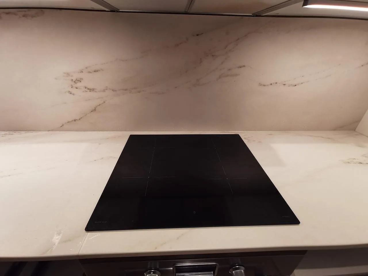 Övermonterad induktionshäll på en matt köksbänkskiva i Dekton Rem Velvet keramik med ljus grå ådring och uppvikt stänkskydd i ett kök i Limhamn.