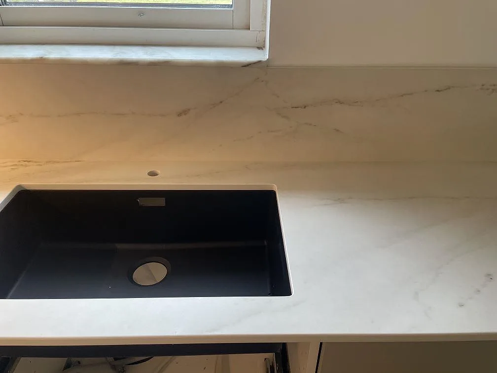 Underlimmad svart kompositdiskho i en köksbänkskiva av matt Dekton Rem Velvet vid fönstret i ett kök i Malmö.