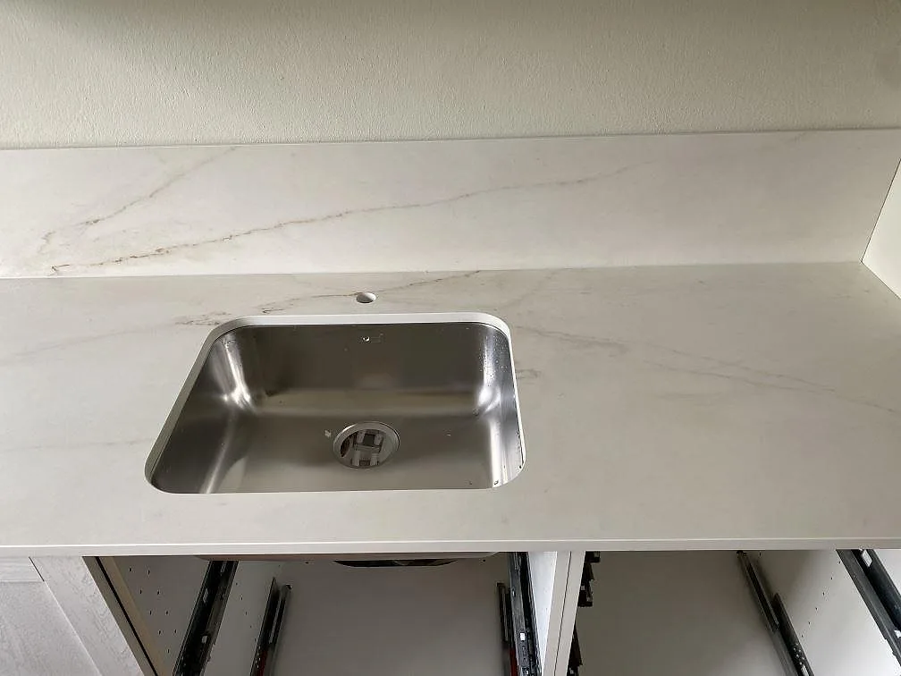 Underlimmad rostfri diskho i en matt köksbänkskiva av Dekton Rem Velvet med ljus ådring och stänkskydd i Malmö.
