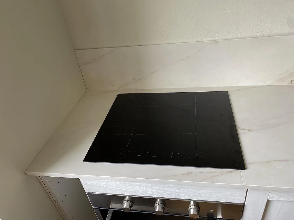 Svart induktionshäll monterad i en matt köksbänkskiva av Dekton Rem Velvet med matchande stänkskydd i Malmö.