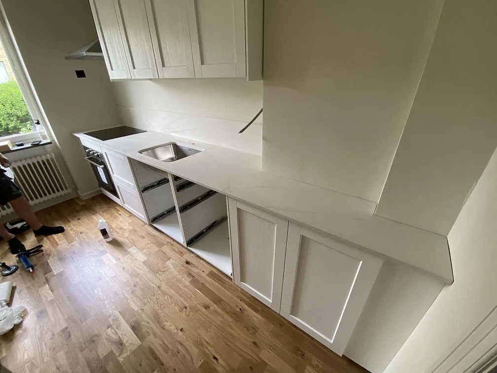 L-formad köksbänkskiva i vit Dekton Rem Velvet, matt keramik, med svart induktionshäll och rostfri diskho under montering i Malmö.