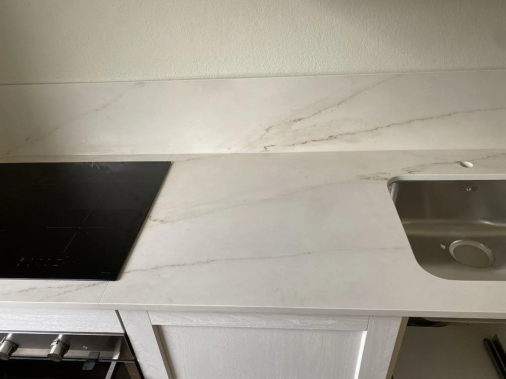 Närbild av matt Dekton Rem Velvet som köksbänkskiva i keramik med svart häll, rostfri diskho och stänkskydd i Malmö.