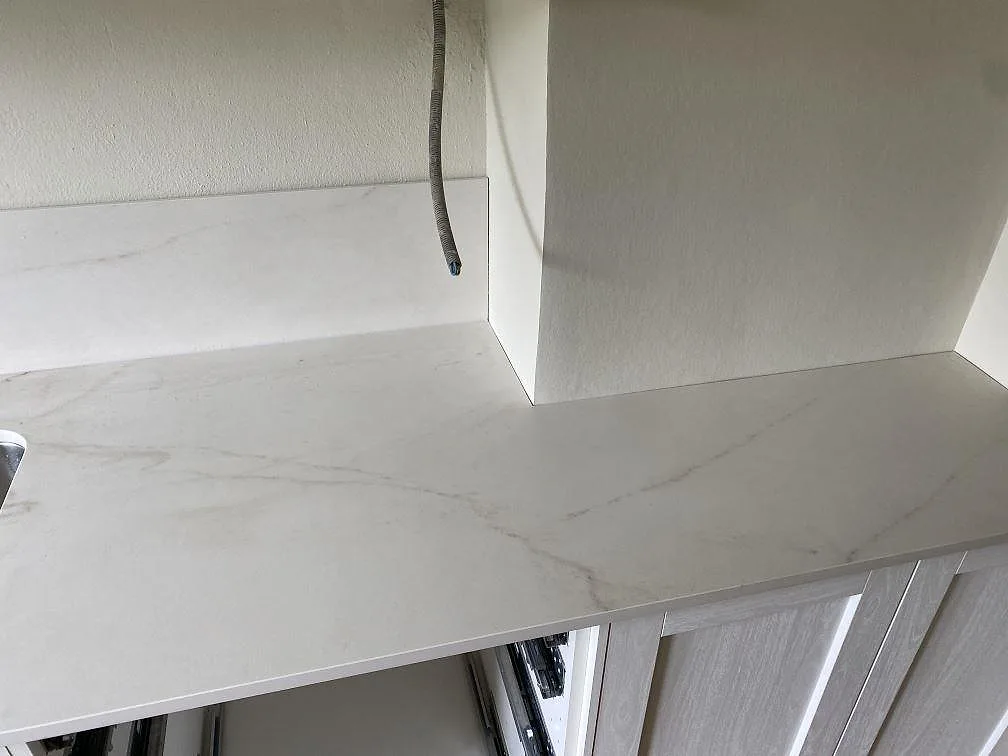 Rak del av köksbänkskiva i matt Dekton Rem Velvet med ljus marmorådring och stänkskydd vid vita köksstommar i Malmö.