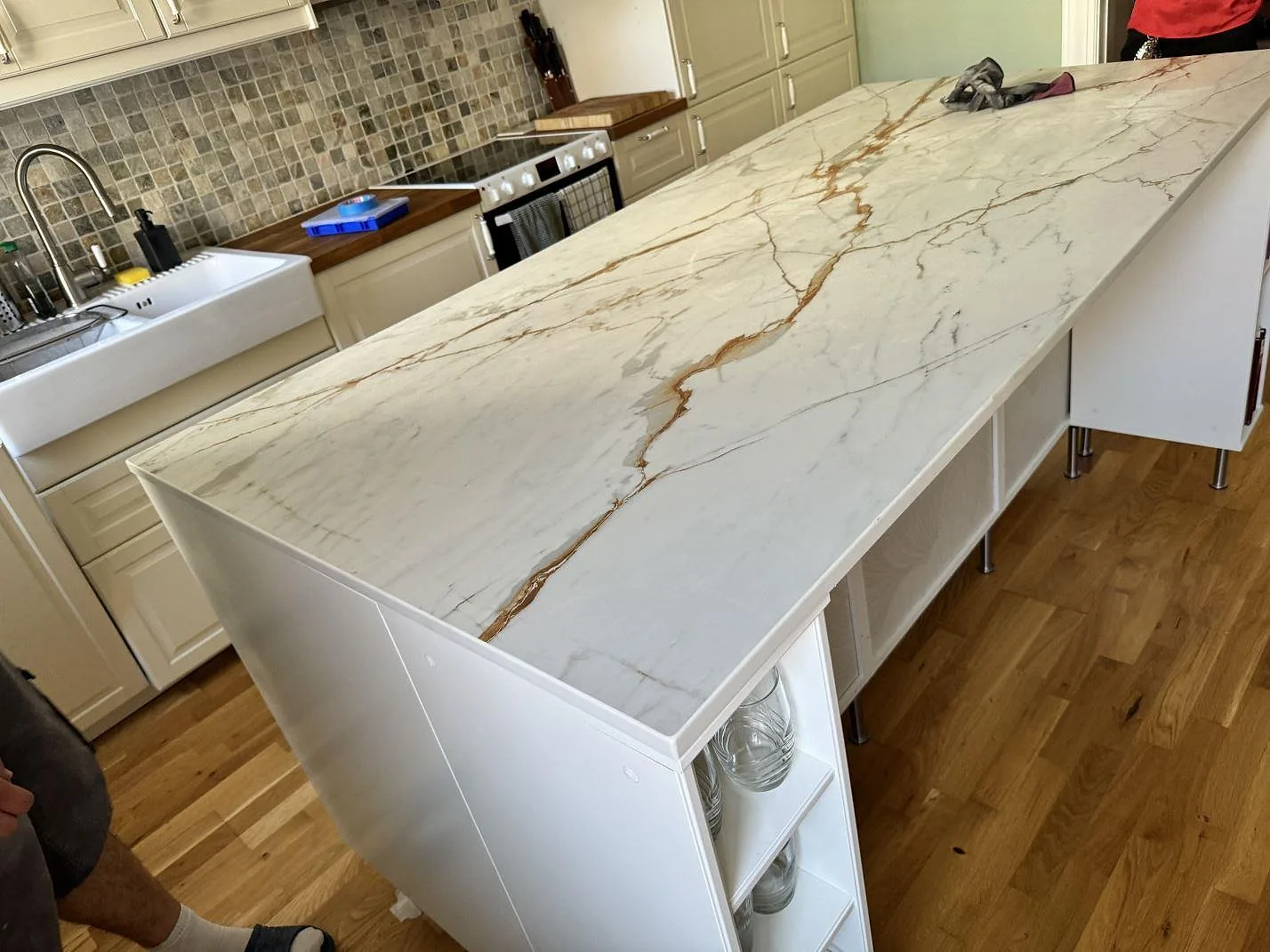 Köksö med bänkskiva i matt Dekton Reverie, vit keramik med guldbrun ådring och neddragen gavelsida i ett kök i Malmö.