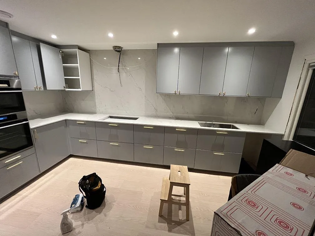 Köksbänkskiva i polerad vit Dekton Salina med matchande stänkskydd och hällöppning i ett grått kök i Hässelby.