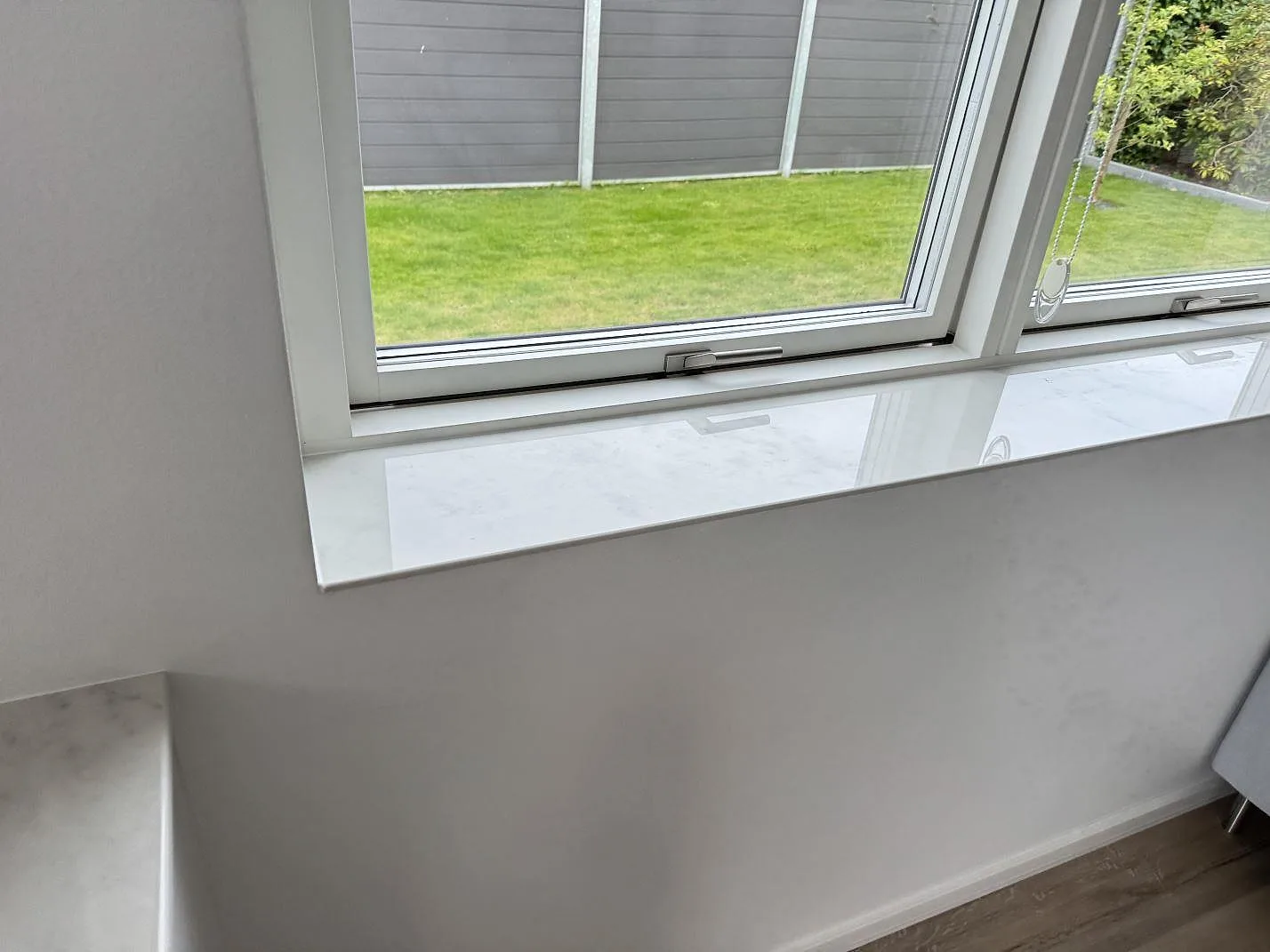 Fönsterbänk i polerad Dekton Salina keramik med ljus grå ådring vid fönster i Ishøj.