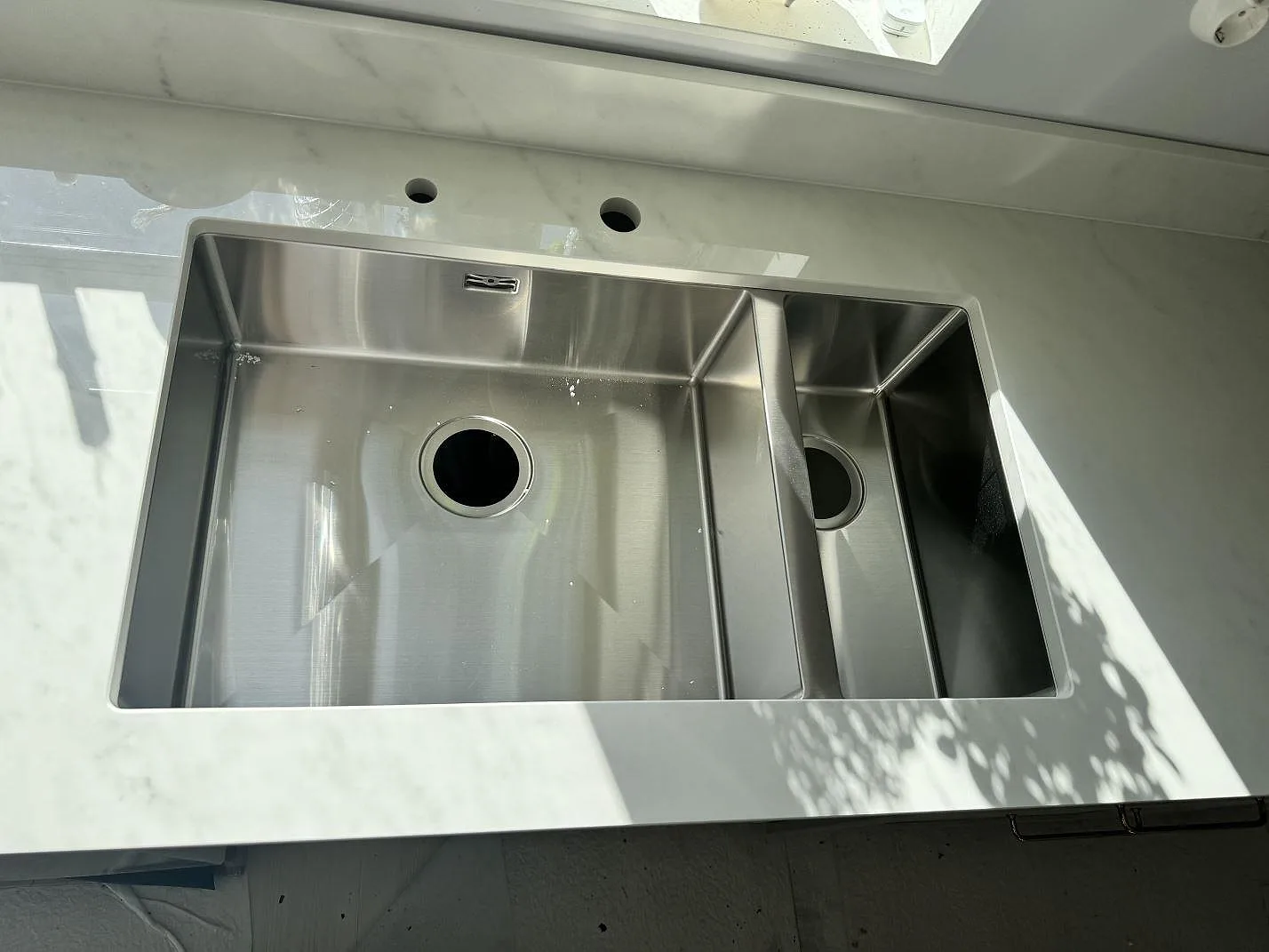 Närbild på underlimmad dubbel rostfri diskho i polerad Dekton Salina keramik med synliga hål för blandare i Sävedalen.