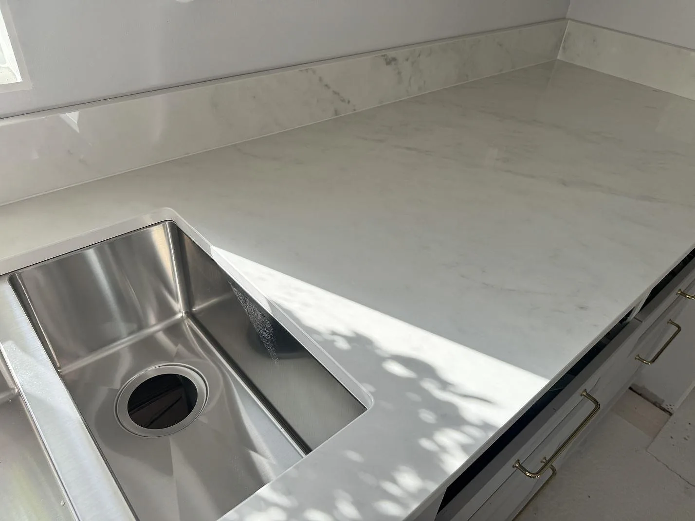 Polerad köksbänkskiva i Dekton Salina keramik med låg stänkkant, vit köksinredning och rostfri diskho i Sävedalen.
