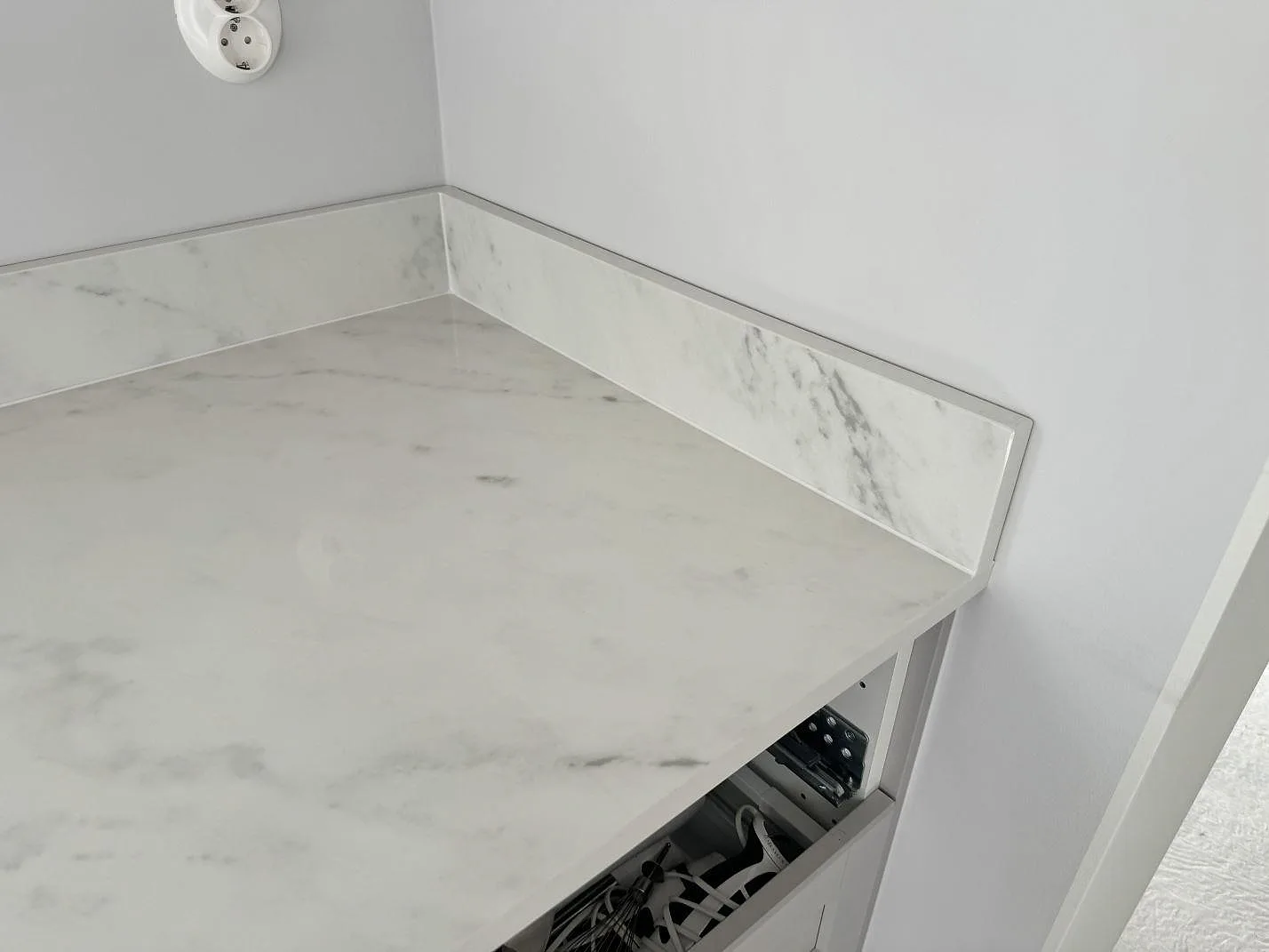 Hörndetalj av köksbänkskiva i polerad Dekton Salina keramik med uppvikt stänkkant och öppen montering i Sävedalen.