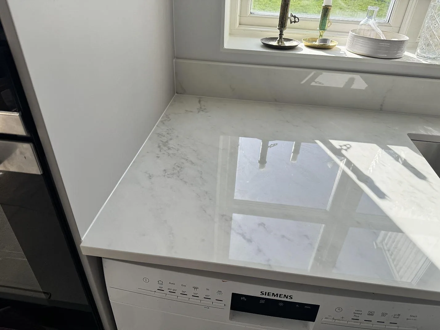 Polerad Dekton Salina keramik som ljus köksbänkskiva vid fönster, med låg stänkkant och vit marmorerad ådring i Sävedalen.