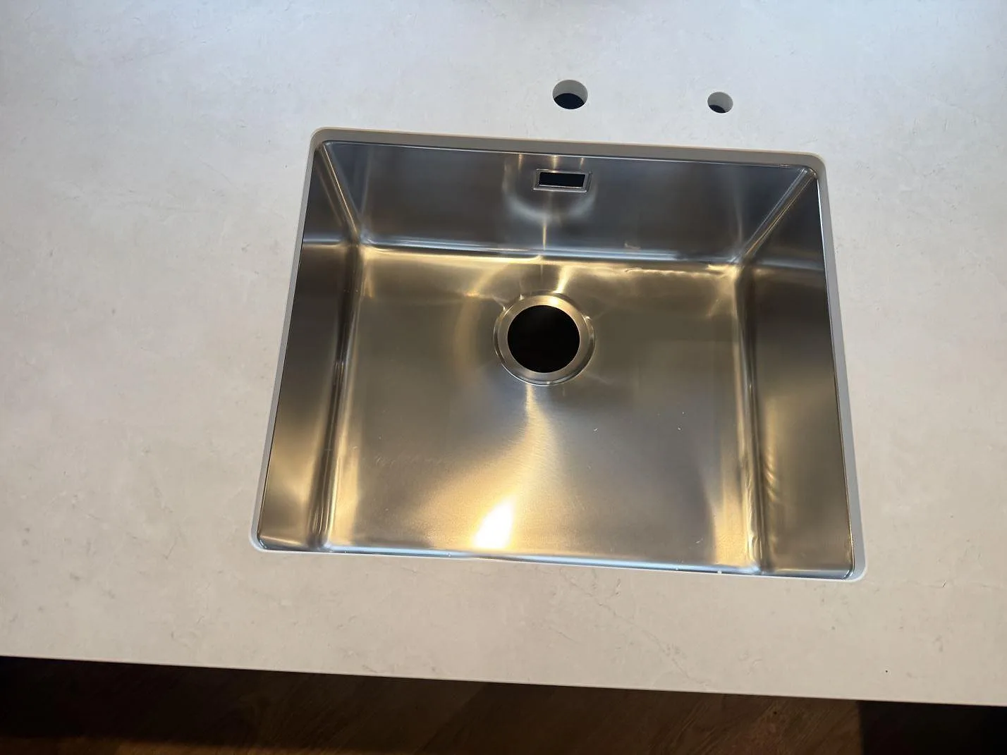 Detalj av rostfri diskho i matt Dekton Sandik bänkskiva med blandarhål i ett kök i Kgs Lyngby.