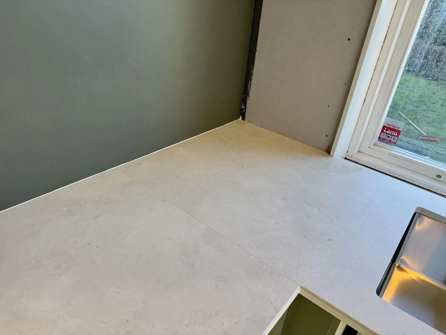 Hörndel av köksbänkskiva i matt Dekton Sandik med ljus stenlik yta och diskho intill fönster i Malmö.