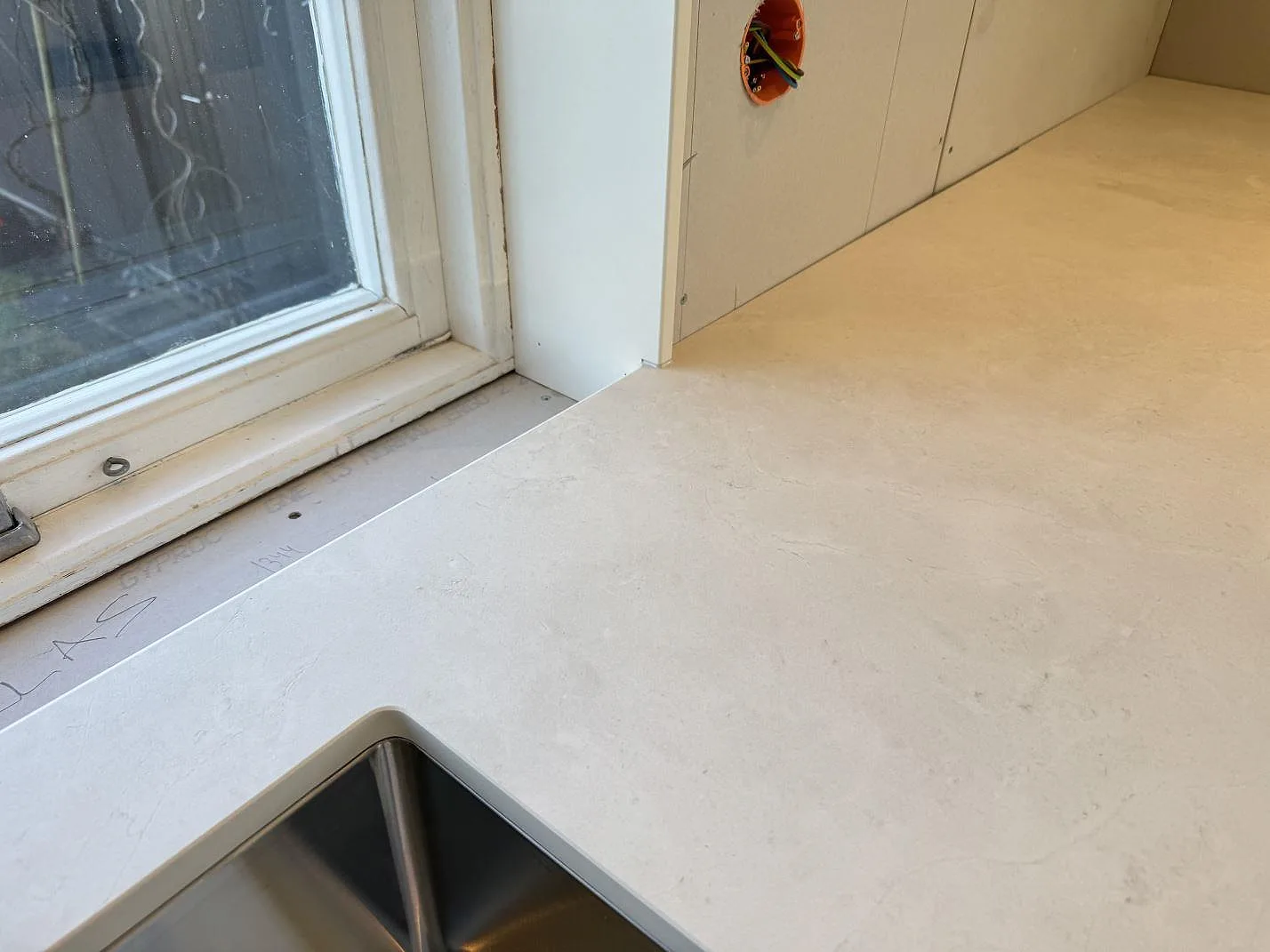 Lång arbetsyta i matt Dekton Sandik, ljus keramisk köksbänkskiva med diskho under montering i Malmö.