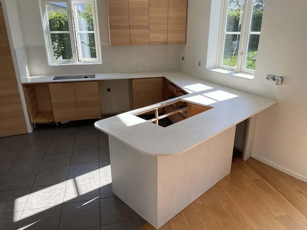 Köksbänkskiva i Dekton Sandik, matt keramik, med U-formad arbetsyta och stänkskydd i ett ljust kök i Sollentuna.