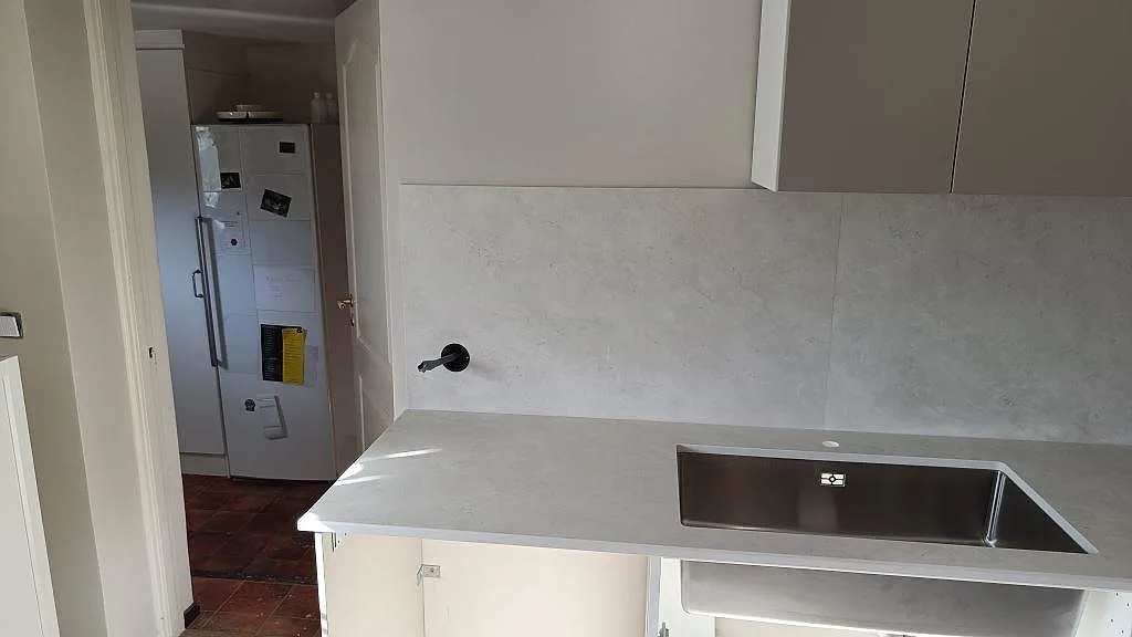 Närbild på matt Dekton Sandik som köksbänkskiva och stänkskydd med rostfri diskho i ett kök under montering i Vellinge.
