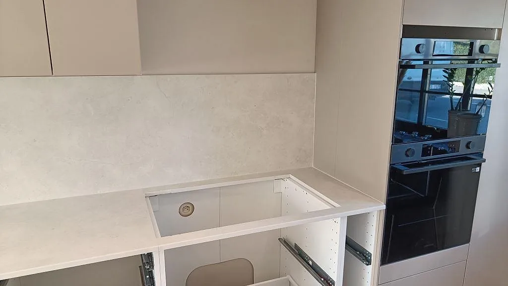 Köksbänkskiva i matt Dekton Sandik keramik med förberett urtag, stänkskydd och inbyggnadsugnar i ett kök i Vellinge.