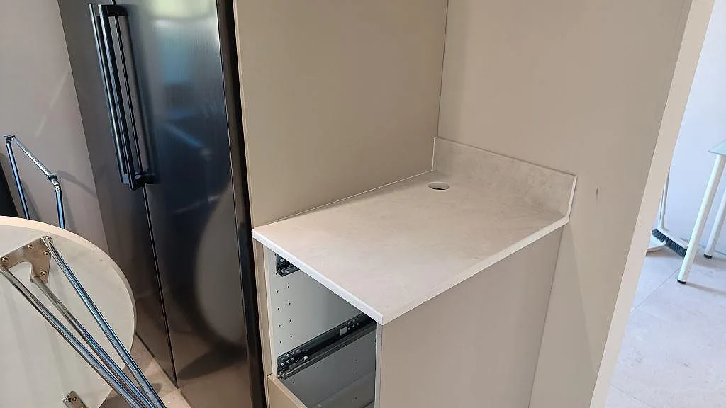 Mindre avställningsyta i matt Dekton Sandik keramik med uppvikt stänkkant och rund genomföring vid kyl i Vellinge.