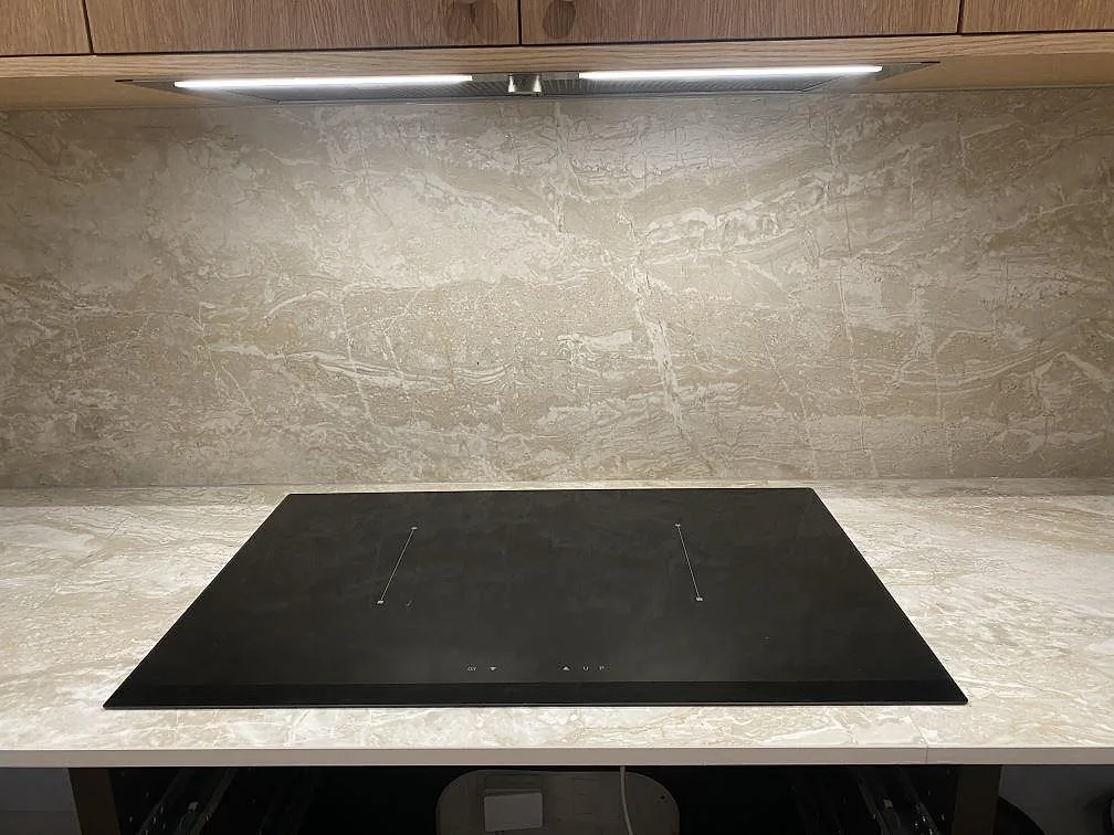 Infälld svart induktionshäll i en matt Dekton Sarey bänkskiva mot ett heltäckande stänkskydd i samma sten i ett kök i Jyderup.