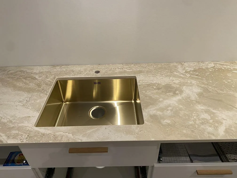 Närbild ovanifrån på den underlimmade mässingsfärgade diskhon i en köksbänkskiva av matt Dekton Sarey i Jyderup.