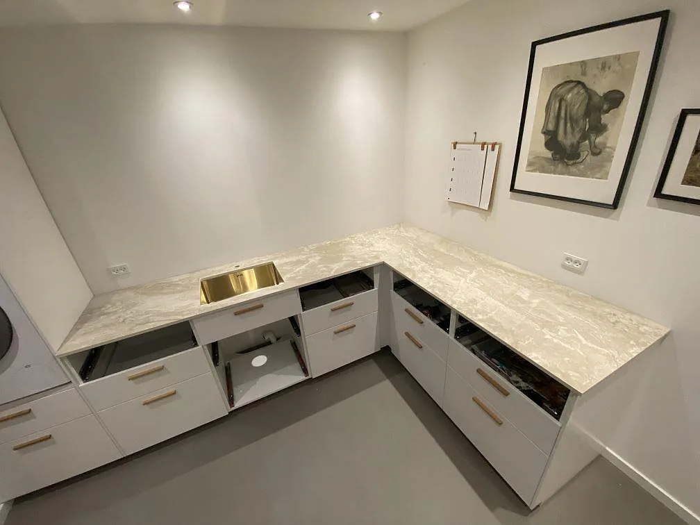Översikt över ett L-format kök i Jyderup med köksbänkskiva i matt Dekton Sarey och en underlimmad borstad mässingsfärgad diskho, fotograferat under montering.