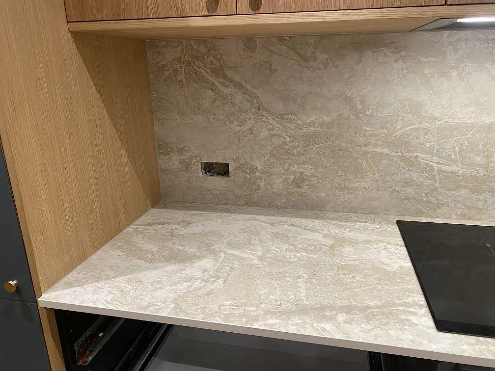 Köksbänkskiva i Dekton Sarey, matt ljus sten med varmgrå och guldaktig ådring, med uppvikt stänkskydd och infälld induktionshäll i ett kök i Jyderup.