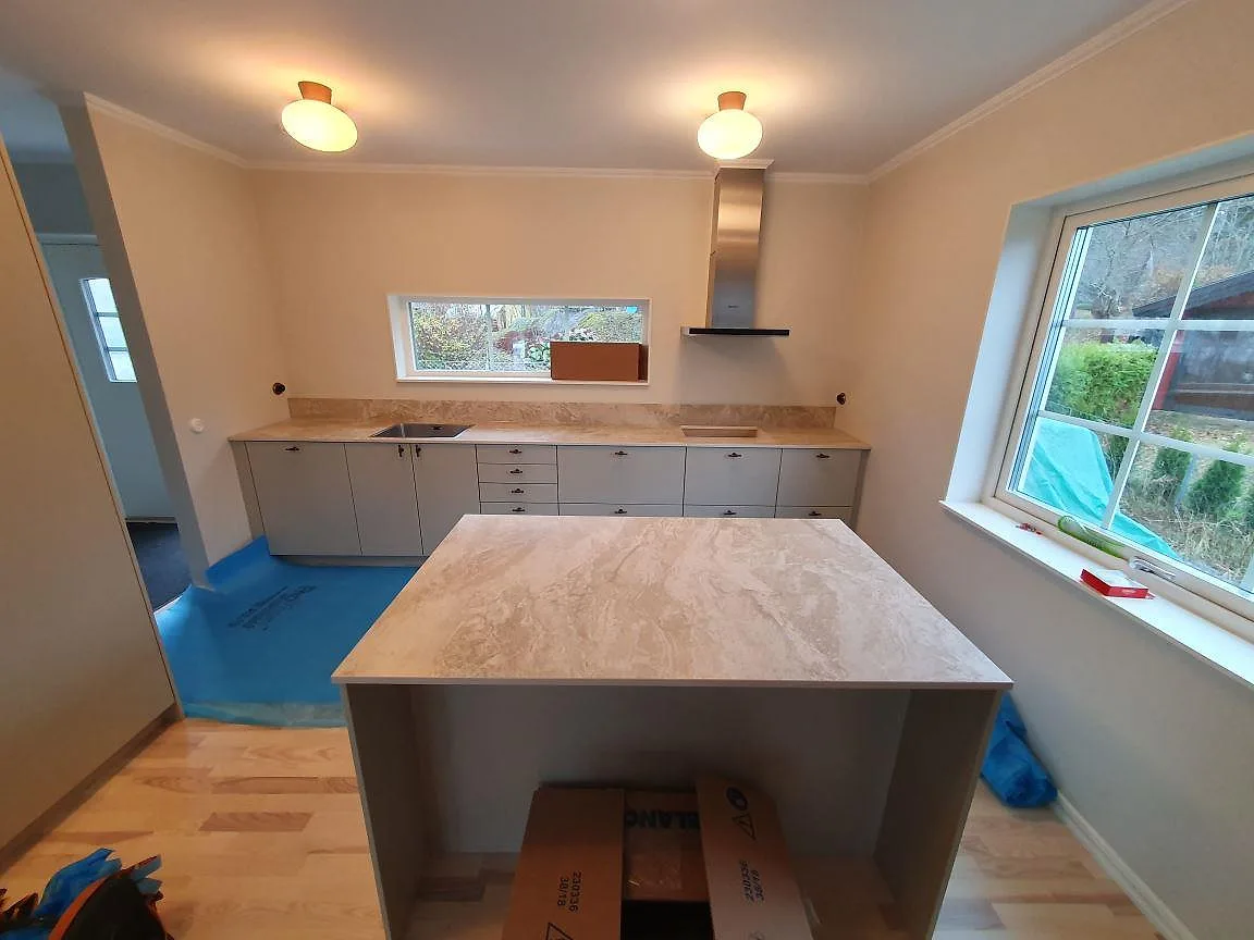 Köksbänkskiva och stor köksö i beige Dekton Sarey, matt keramik, i ett kök under montering i Segeltorp.
