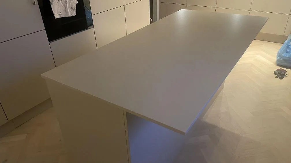 Köksö med bänkskiva i matt Dekton Sasea, ljusgrå keramik, sedd från gaveln i ett kök i Åkarp.