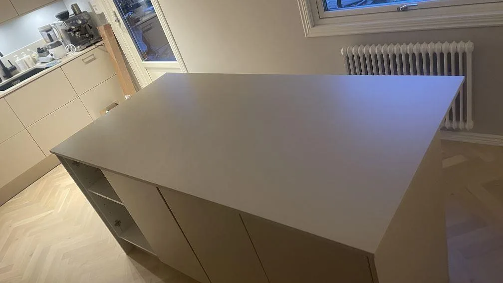 Stor köksö med matt köksbänkskiva i Dekton Sasea, keramik, framför fönster i ett kök i Åkarp.