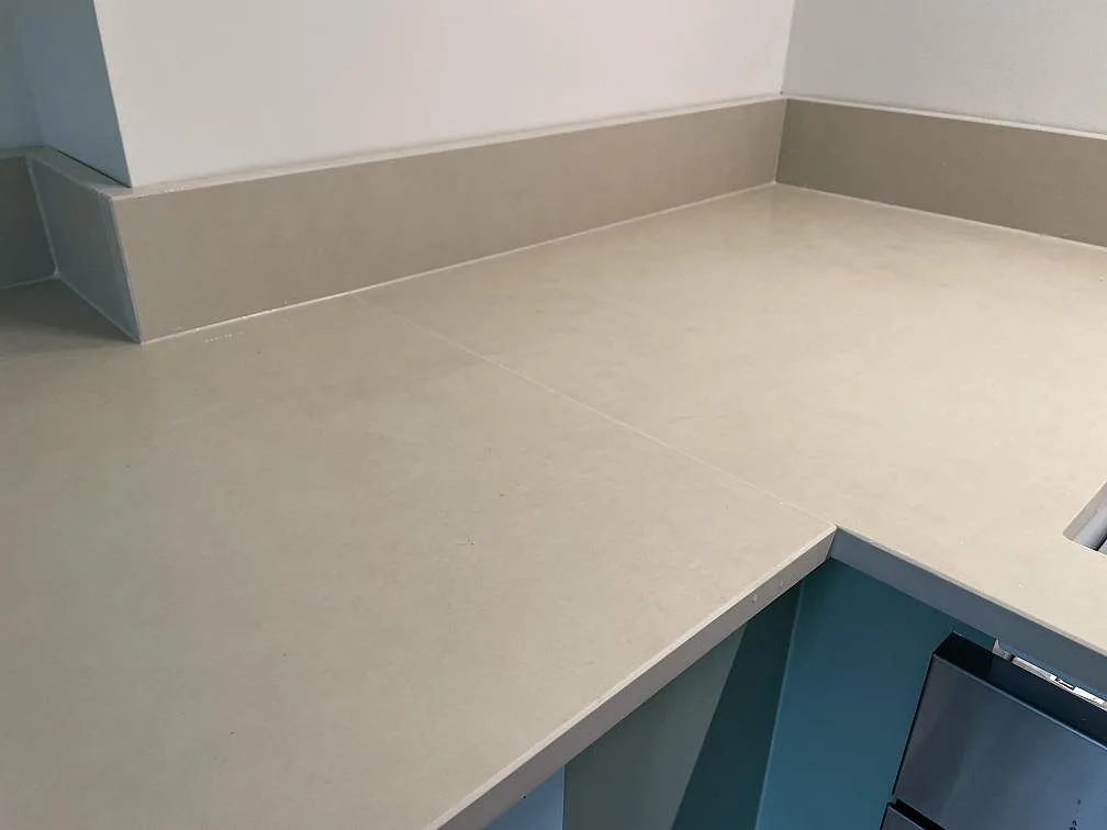 Hörn på L-formad köksbänkskiva i matt Dekton Sasea keramik med sagegröna köksstommar och låg stänkkant i Malmö.