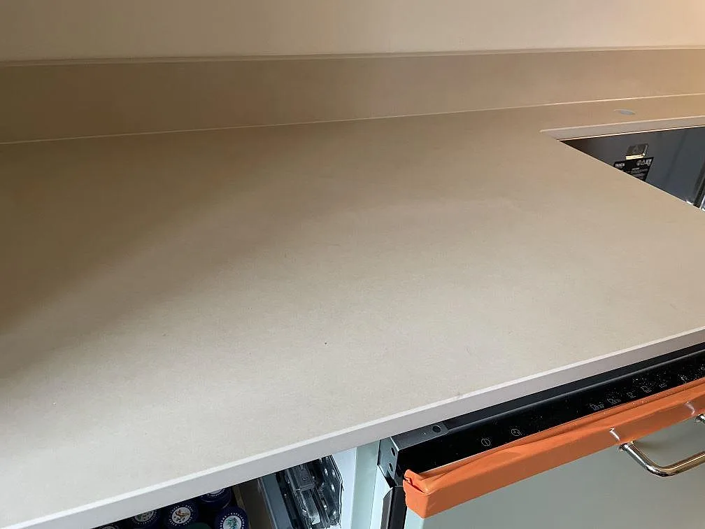 Detalj av den matta Dekton Sasea bänkskivan i Malmö med svart induktionshäll, beige keramikyta och underlimmad diskho i bakgrunden.