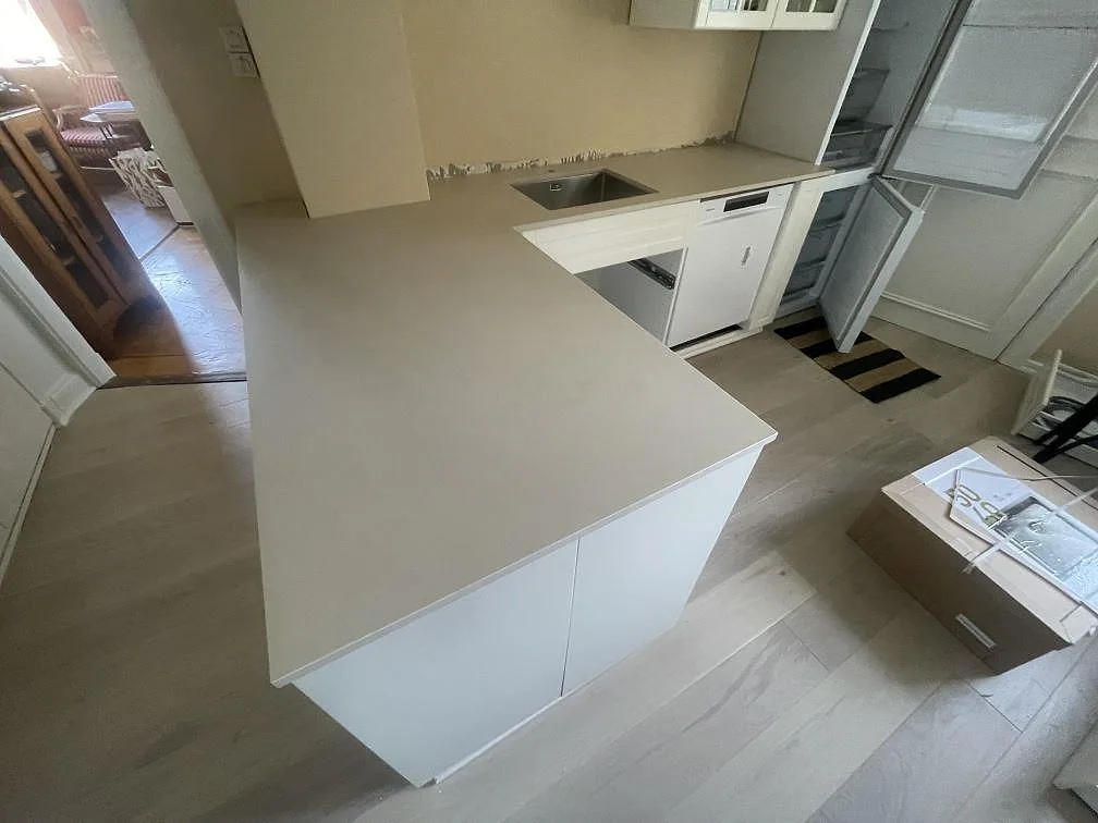 U-formad köksbänkskiva i matt Dekton Sasea, keramik, med underlimmad diskho och vit köksinredning i Södertälje.