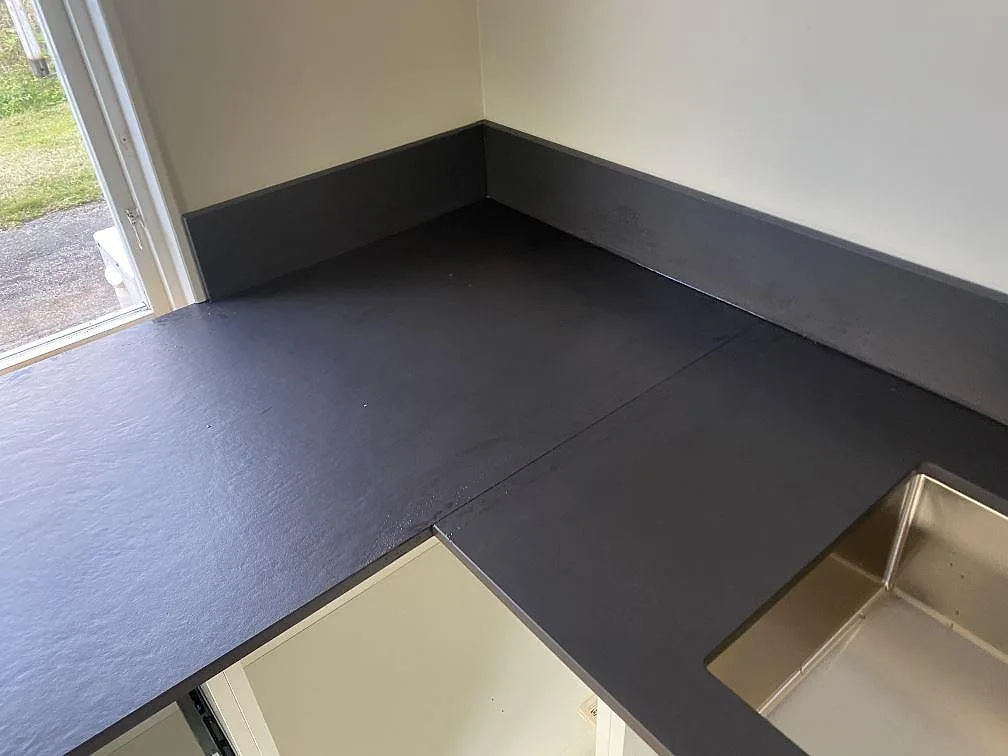 Hörnbänk i mörkgrå Dekton Sirius, matt, med uppvikt stänkkant och plats för diskho i ett kök i Ängelholm.