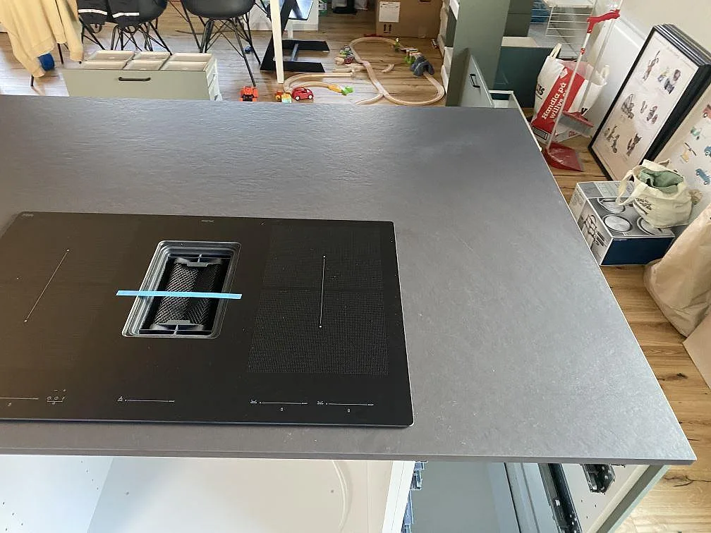 Köksö i Dekton Sirius, matt mörk yta, med infälld induktionshäll och integrerad fläkt i ett kök i Ängelholm.