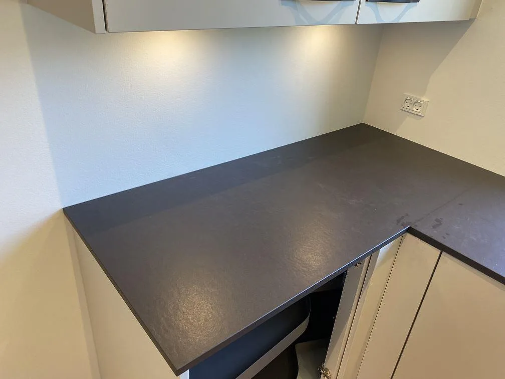Hörndel av köksbänkskiva i mörk matt Dekton Sirius, 20 mm keramik, monterad under överskåp i Brønshøj.
