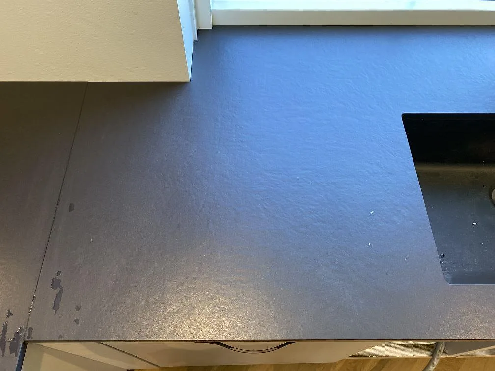 Detalj av matt Dekton Sirius-bänkskiva vid diskplatsen, med mörk keramisk yta och diskho längs fönsterväggen i Brønshøj.