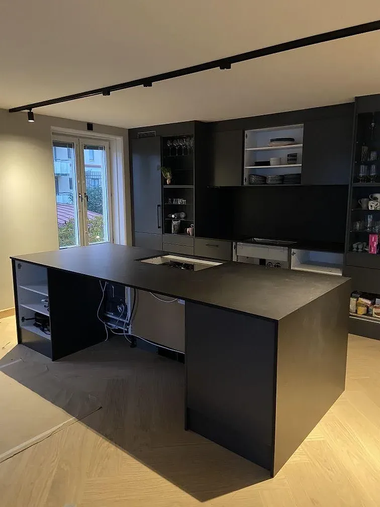 Köksö i mörk grafitgrå Dekton Sirius med infälld häll, i ett svart kök med ljus fiskbensparkett i Göteborg.