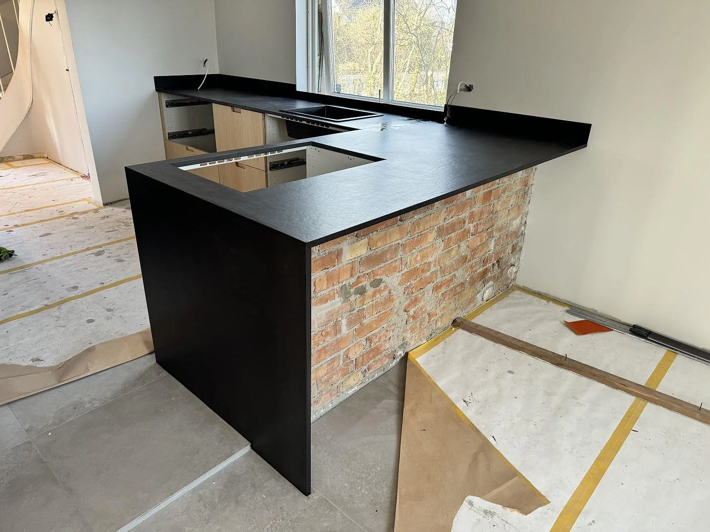 L-formad köksbänkskiva i matt Dekton Sirius keramik med hällöppning, diskho och mörk gavelsida mot tegel i Höganäs.