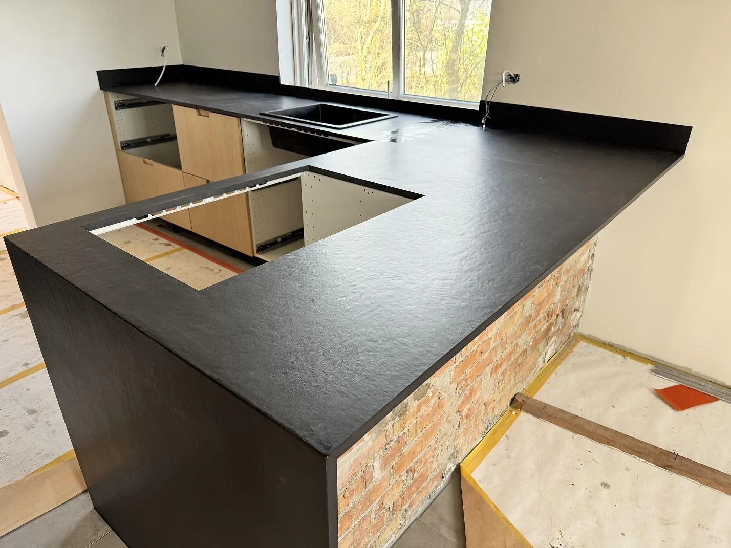 Matt Dekton Sirius köksbänkskiva med hällöppning, fönsterparti, stänkkant och synlig mörk keramikyta i Höganäs.