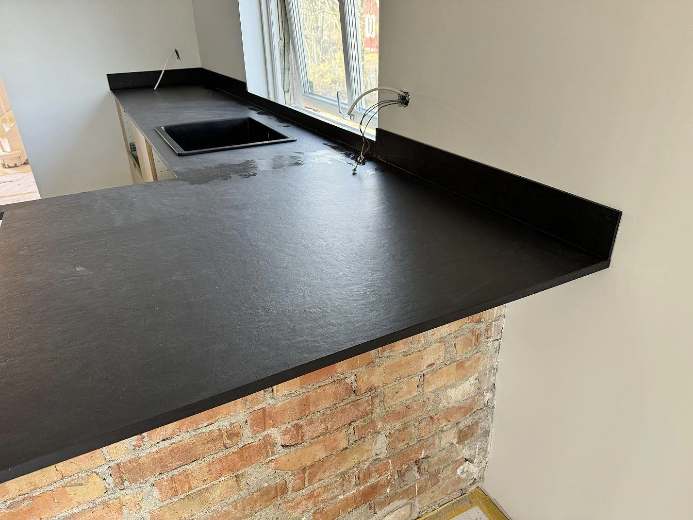 Närbild av matt Dekton Sirius som köksbänkskiva med stänkkant, fönsterbänk och diskho i ett kök i Höganäs.