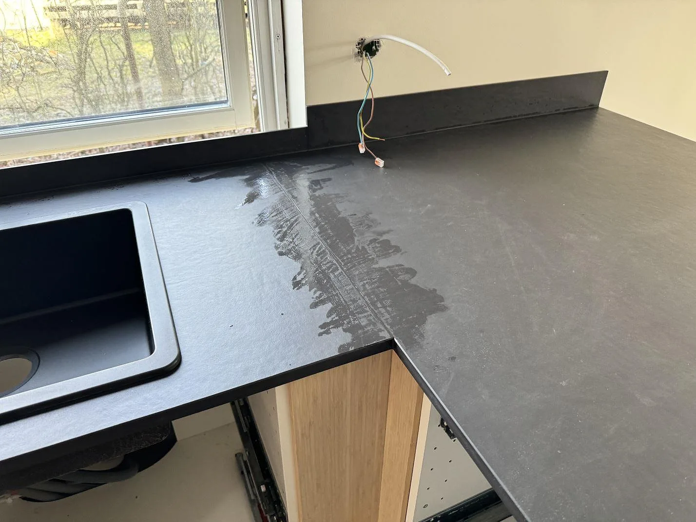 Hörn i matt Dekton Sirius med diskho, fönsterbänk, stänkkant och eldragning under montering i Höganäs.