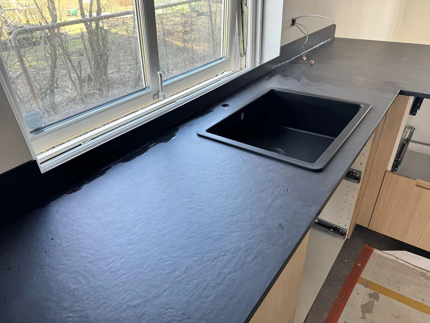 Köksbänkskiva i matt Dekton Sirius med fyrkantig mörk diskho, fönsterbänk och stänkkant i Höganäs.