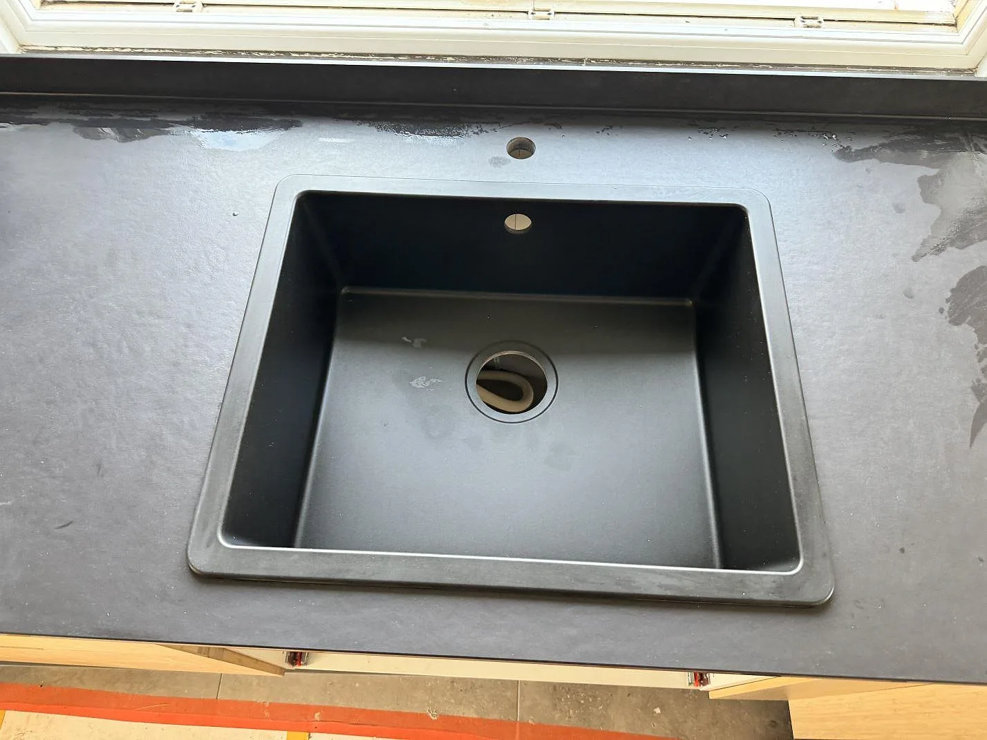 Detaljbild av fyrkantig diskho i en matt Dekton Sirius köksbänkskiva under fönstret i Höganäs.