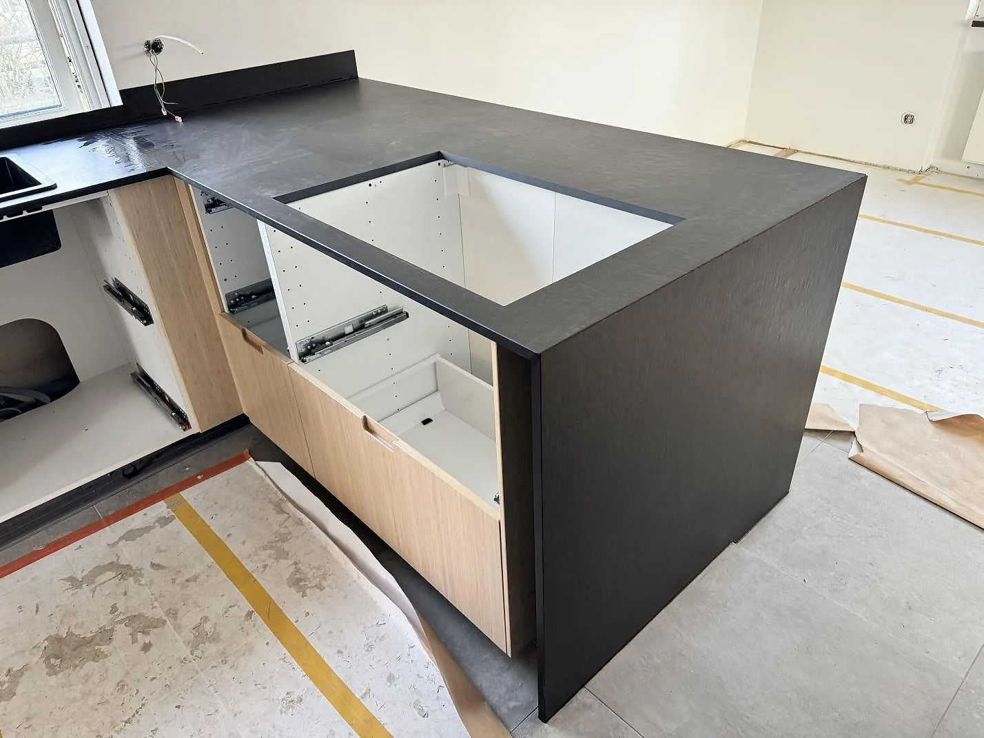 Köksbänkskiva i matt Dekton Sirius med hällöppning, uppvikt stänkkant och ljusa köksstommar under montering i Höganäs.