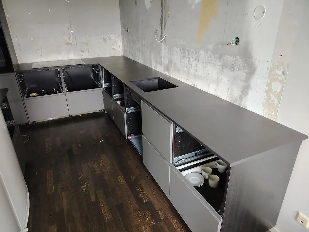 Köksbänkskiva i mörkgrå Dekton Sirius, matt, med induktionshäll i ett U-format kök under montering i Järfälla.