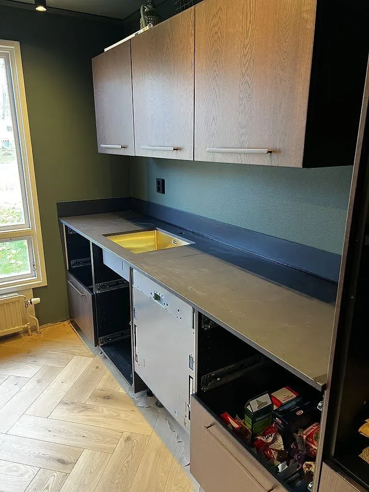 Köksbänkskiva i matt Dekton Sirius med mässingsfärgad diskho och öppna köksstommar under montering i Karlshamn.