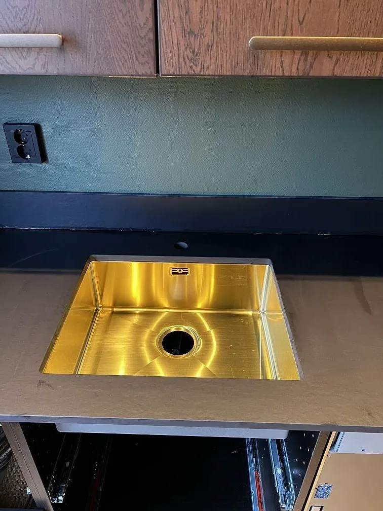 Detalj av mässingsfärgad diskho i en mörk matt Dekton Sirius keramikbänkskiva i ett kök under montering i Karlshamn.