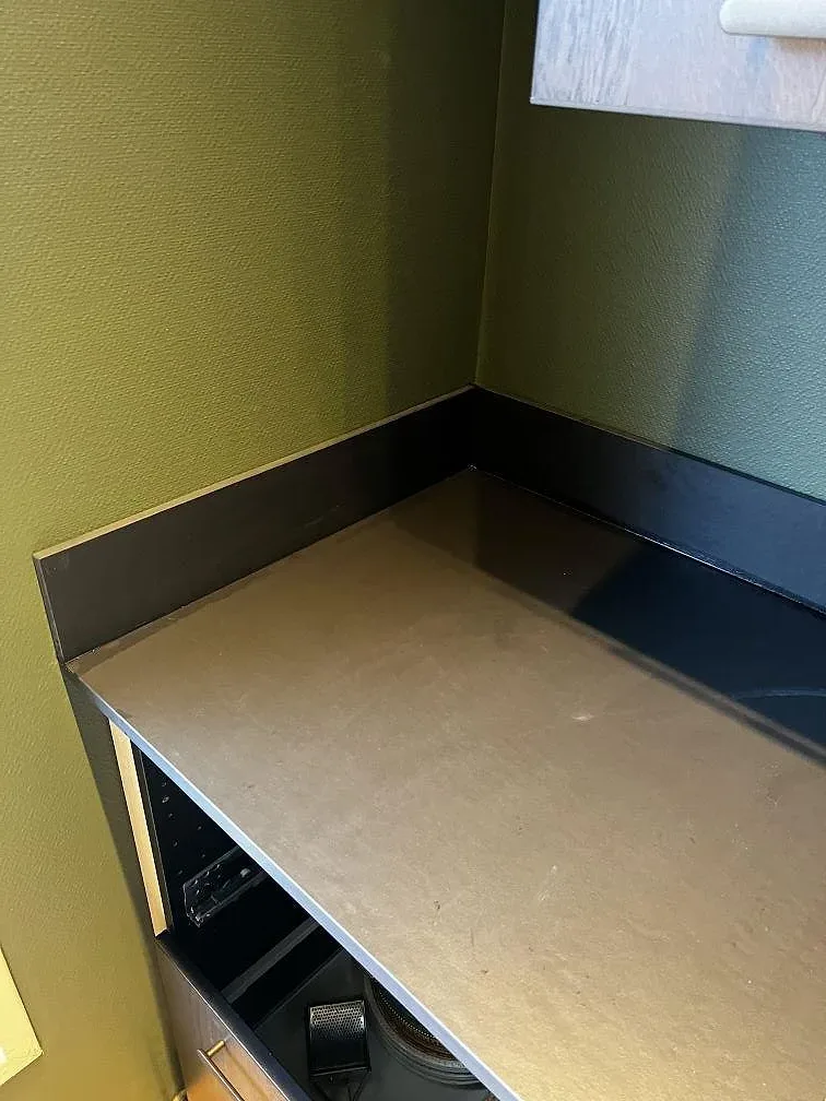 Detalj av mörk matt Dekton Sirius längs väggbänk och kantprofil, med gröna väggar i ett kök i Karlshamn.