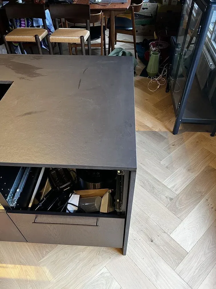 Sidovy av köksö klädd med mörk matt Dekton Sirius, med synliga stenkanter och fiskbensgolv i ett kök i Karlshamn.