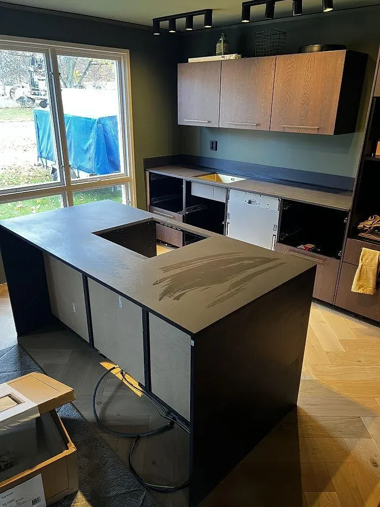 Mörk matt köksbänkskiva i Dekton Sirius på köksö och väggbänk, fotograferad med gröna väggar och ljust fiskbensgolv i Karlshamn.