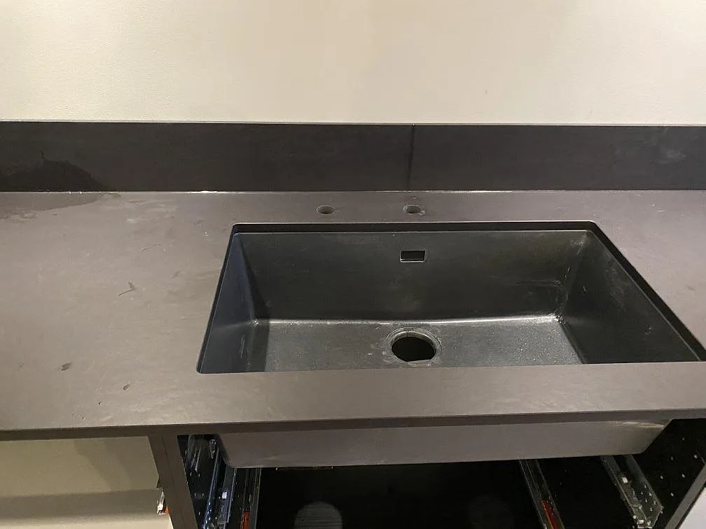 Köksbänkskiva i nästintill svart Dekton Sirius med underlimmad mörk diskho och uppvikt stänkkant i ett kök i Oxie.